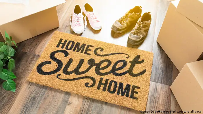 Doormat that says Home Sweet Home with two pairs of shoes behind it. 