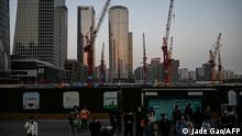 People wait for buses at a bus stop near a construction site at central business district in Beijing on March 26, 2023. (Photo by Jade Gao / AFP)