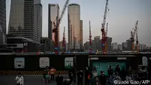 People wait for buses at a bus stop near a construction site at central business district in Beijing on March 26, 2023. (Photo by Jade Gao / AFP)