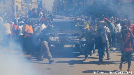 Raila Odinga's car convoy in the middle of a protesting crowd, surrounded by smoke from tear gas cartridges