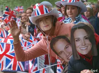 Royal fans wearing a Kate Middleton mask, a Prince William mask and a Queen Elizabeth mask wait for the wedding cortege to pass by