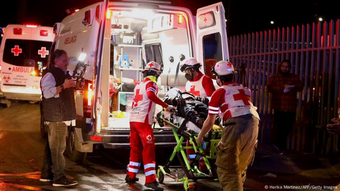 Sanitäter schieben eine Bare mit einer verwundeten Person in einen Rettungswagen, ein Mann filmt die Szene