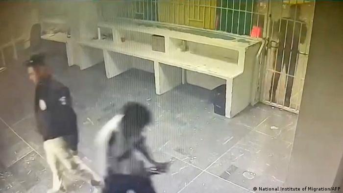Ein Bild aus dem Video zeigt eine Person hinter einem gefängnisartigen Gitter, hinter ihm ist ein Feuer zu erahnen, vor dem Gitte: zwei abgewandte Uniformierte 