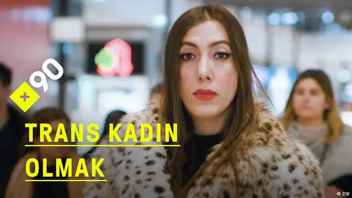 Zu sehen ist Berfin, eine trans*Frau, die in der Folge Was bedeutet es, eine trans Frau zu sein? des türkischsprachigen DW-Formats, porträtiert wird. Berfin ist geschminkt, hat lange, glatte braune Haare, die sie in offen trägt. Ihr Plüschmantel ist im Leopardenmuster.