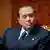 Silvio Berlusconi sits in a gold-backed chair