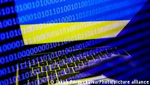 Ukrainian flag displayed on a laptop screen and binary code code displayed on a screen are seen in this multiple exposure illustration photo taken in Krakow, Poland on February 16, 2022. (Photo illustration by Jakub Porzycki/NurPhoto)