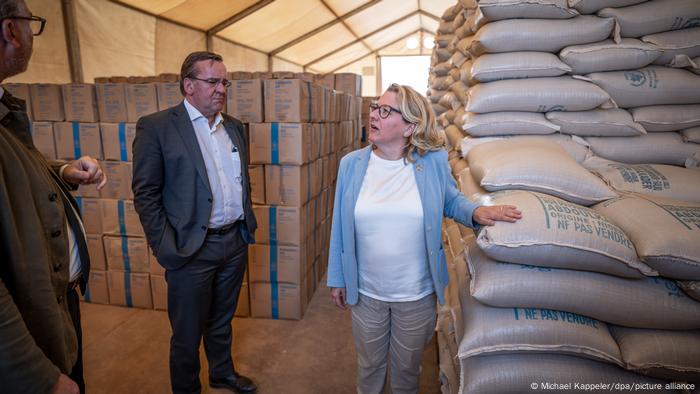 Die deutschen Minister Pistorius und Schulze stehen in einem Lagerhaus des UN Welternährungsprogramms vor Getreidesäcken