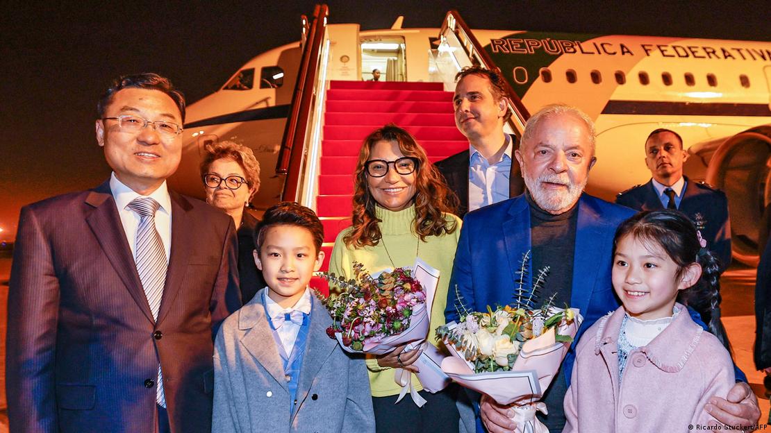 Janja e Lula recebem flores ao desembarcarem em Xangai, na China. Dilma Rousseff é vista ao fundo.
