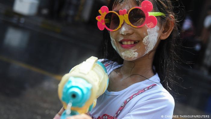 Una chica en una calle de Bangkok dispara con una gran pistola de agua mientras lleva pintura blanca en la cara.