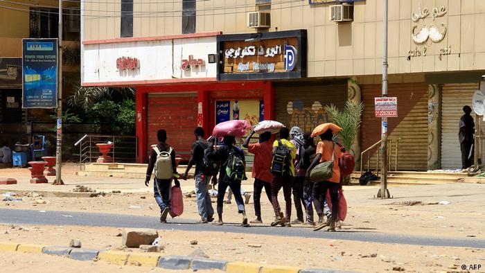 Eine kleine Gruppe Zivilisten mit Rucksäcken und Bündeln zieht durch die ansonsten leeren Straßen Khartums