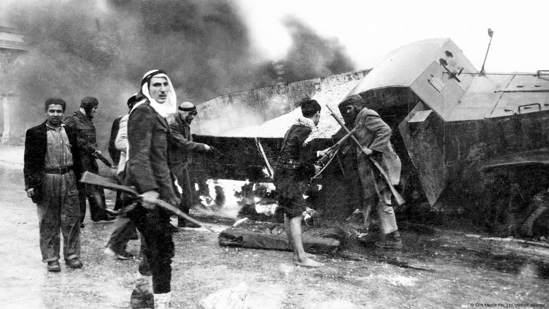 Combatentes palestinos ao lado de um caminhão virado, em foto preto e branco