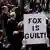 A person holds "Fox Is Guilty" sign as reporters gather in front of Delaware Superior Court