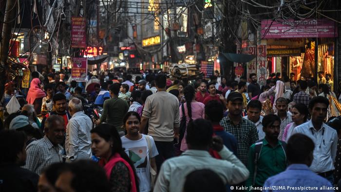 Люди идут близко друг к другу по торговой улице в Нью-Дели, Индия.