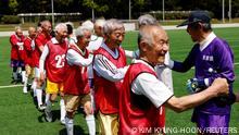 A group of elderly Japanese soccer players bump fists on a field