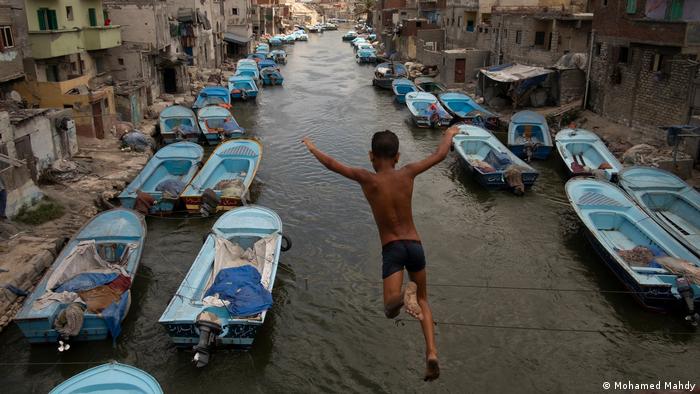 Ein Junge in Badehose springt in einen Kanal voller Fischerboote
