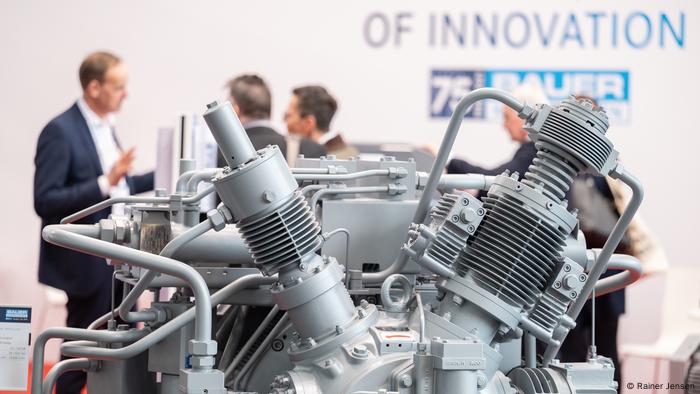 The top half of a compressor, with a group of men standing in the background.  The wall behind them says of Innovation