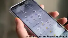 Mão segurando smartphone com aplicativo de meteorologia 