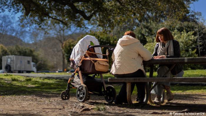 La mujer, con un carrito de bebé, sentada de espaldas a la cámara en un banco de un parque.