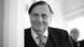 Barry Humphries, in three-piece suit and tie, smiles into the camera as he leans against a doorframe Barry Humphries, in three-piece suit and tie, smiles into the camera as he leans against a doorframe