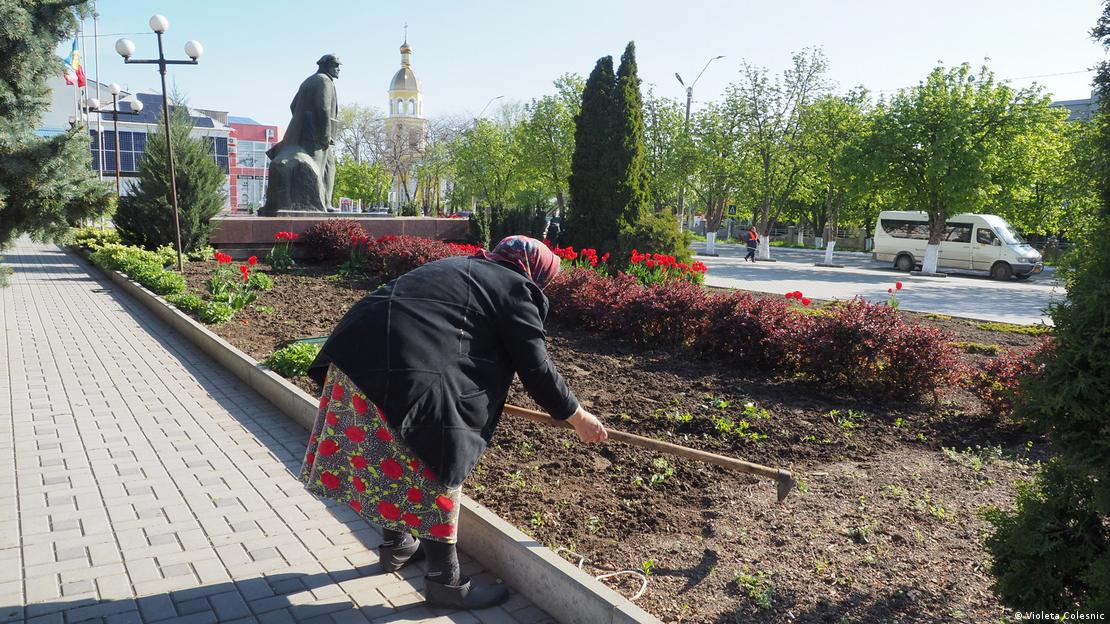 A woman rakes a flowerbed while a statue of Lenin can be seen in the background