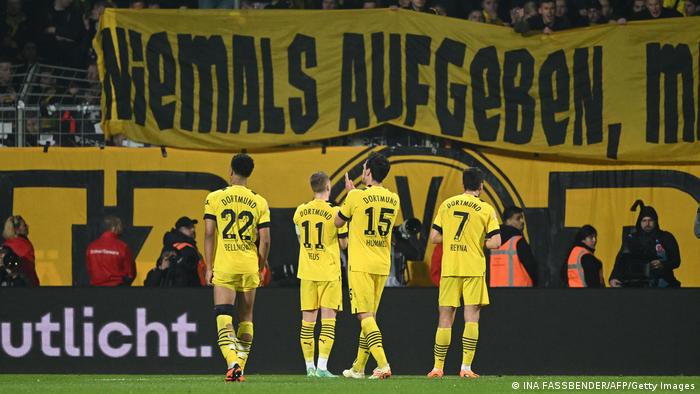Jude Bellingham, Marco Reus, Mats Hummels und Giovanni Reyna (l.-r.) applaudieren der Dortmunder Südkurve mit dem Banner Niemals aufgeben.