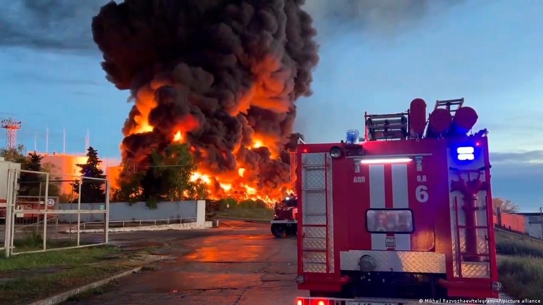 Carro dos bombeiros, com imensas chamas e fumaça ao fundo