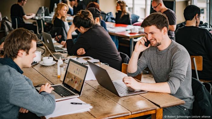 Mehrere Menschen sitzen vor ihren Laptops in einem Coworking Space in einem Café in Berlin Mehrere Menschen sitzen vor ihren Laptops in einem Coworking Space in einem Café in Berlin