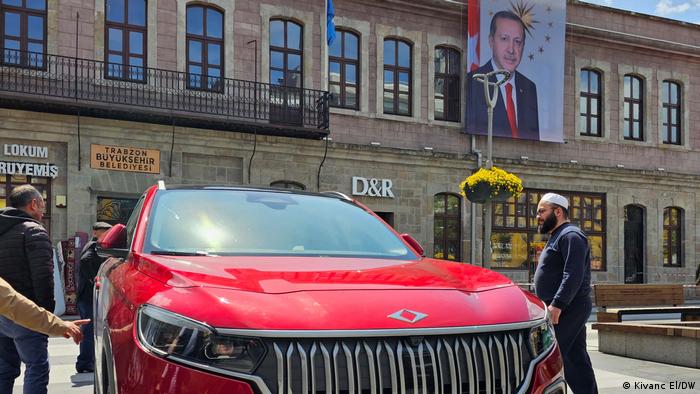Ein rotes E-Auto TOGG, dahinter an einer Hauswand das Porträt Erdogans