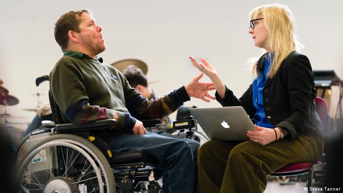 Eine Frau mit einem Laptop unterhält sich mit einem Mann im Rollstuhl