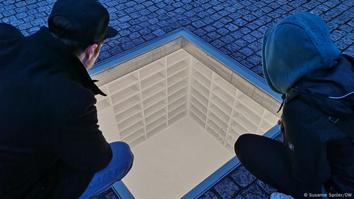 Zwei Personen betrachten das Denkmal zur Bücherverbrennung auf dem Bebelplatz in Berlin