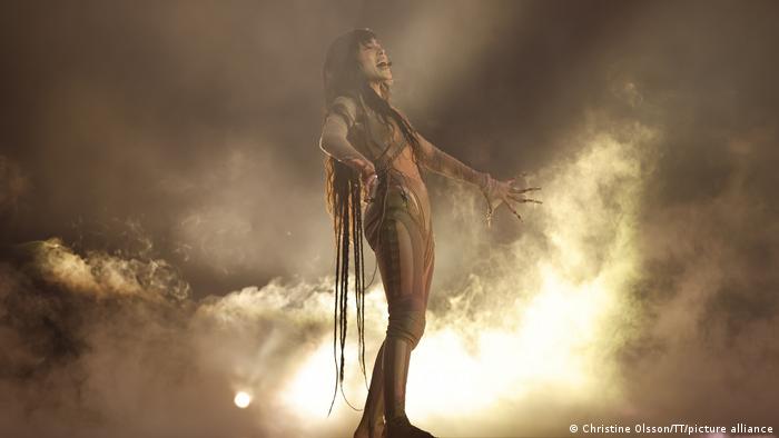 The Swedish singer Loreen stands on the stage, behind her diffused light and smoke.