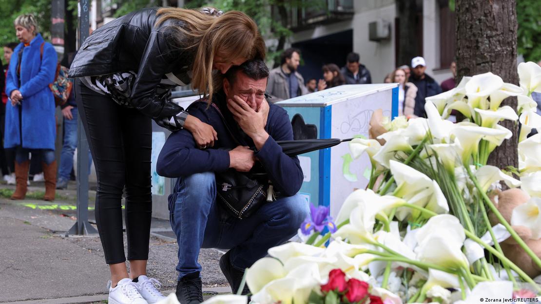 Ein weinender Mann und eine junge Frau vor abgelegten Blumen