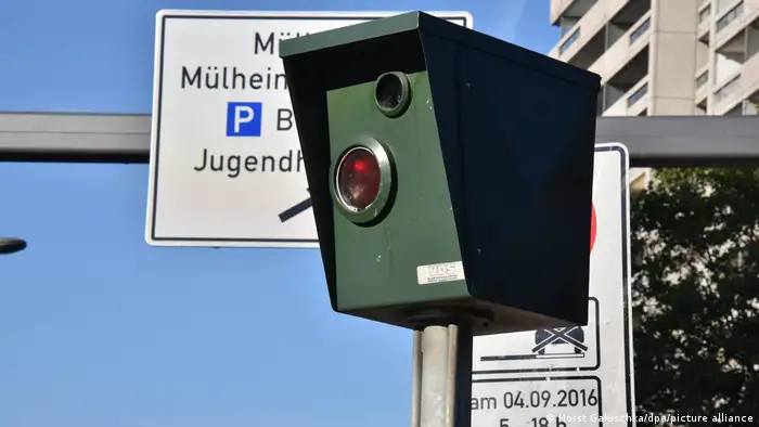 Box-like speed-recorder with traffic signs in the background and a blue sky.