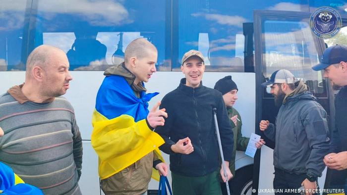 Mehrere Männer vor einem Bus, einer hat die ukrainische Fahne umgelegt