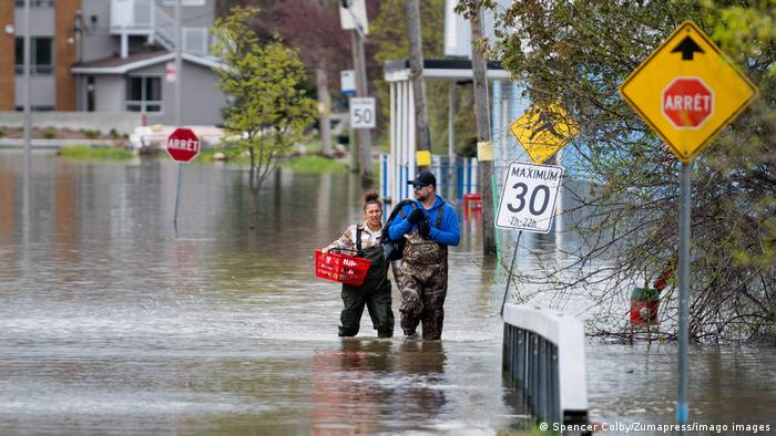 Ein Mann und eine Frau in Anglerhosen waten knietief über eine überflutete Straße.