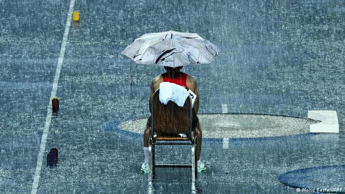 Un deportista tailandés espera debajo de un paraguas, sentado en una silla, a que amaine la lluvia, en Phnom Pen.