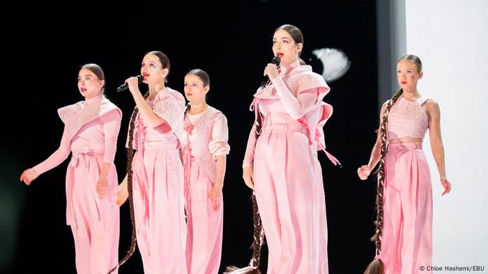 Sechs Frauen in rosa Kleidung singen in Mikrofone.