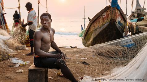 African Fisherman in wooden boat throwing out fishing net Stock