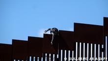 A migrant climbs over the border fence into the United States after fetching groceries for other migrants waiting to be processed by authorities on the US side of the US-Mexico border, as seen from Tijuana, Baja California State, Mexico, May 10, 2023. A surge of migrants is expected at the US-Mexico border cities as President Biden administration is officially ending its use of Title 42. On May 11, President Joe Biden's administration will lift Title 42, the strict protocol implemented by previous president Donald Trump to deny entry to migrants and expel asylum seekers based on the Covid pandemic emergency. (Photo by Guillermo Arias / AFP)