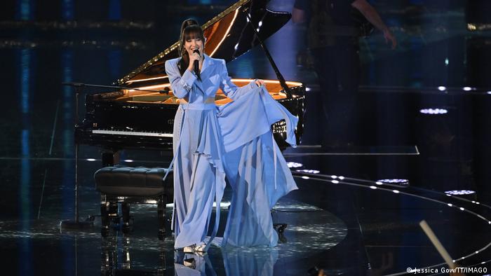 Sängerin auf der Bühne singt in ein Mikrofon, hinter ihr ein Flügel.