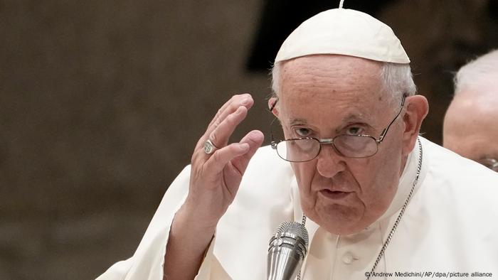 Porträt von Papst Franziskus, der hinter eine Mikrofon steht und die rechte Hand erhoben hat
