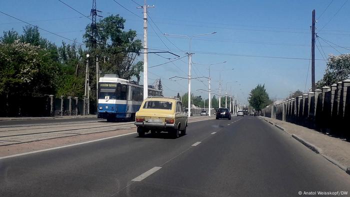 Автомобиль на дороге в Усть-Каменогорске, ведущей в Россию. Приближается трамвай, на заднем плане едут еще машины