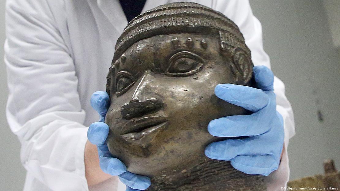 Bronze-Skulptur, gehalten von zwei Händen in blauen Handschuhen, Oberkörper im weißen Kittel