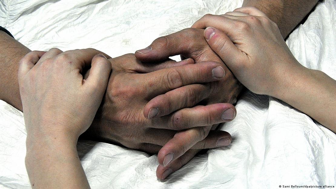 ایک نرس ہمدردی سے ایک لاعلاج مریض کے ہاتھوں پر ہاتھ رکھے ہوئے