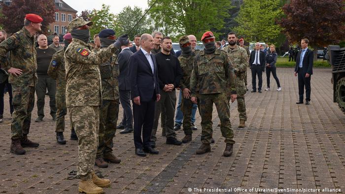 Bundeskanzler Olaf Scholz steht mit Präsident Wolodymyr Selenskyj und Bundeswehrsoldaten auf einem Platz