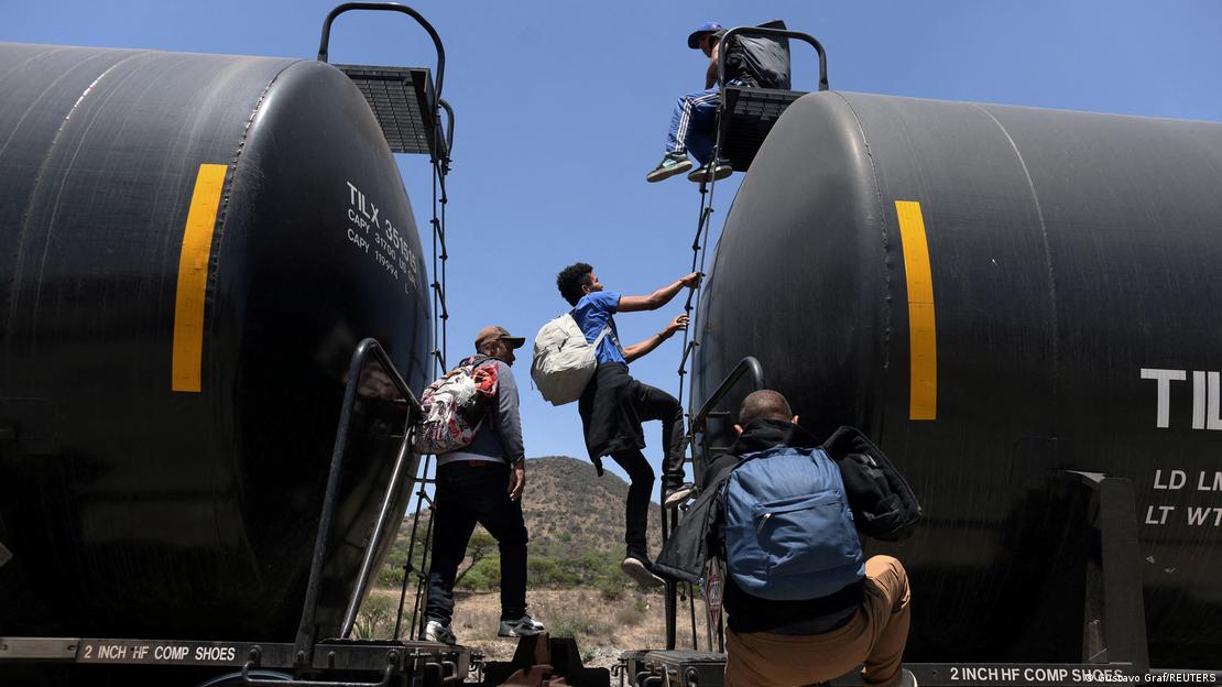 Personas migrantes tratan de cruzar hacia EE. UU. colgándose del vagón de un tren de carga.