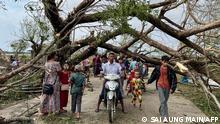 Residents walk past fallen trees in Kyauktaw in Myanmar's Rakhine state on May 15, 2023, after Cyclone Mocha crashed ashore. Cyclone Mocha crashed ashore in Myanmar and southeastern Bangladesh on May 14, uprooting trees, scattering flimsy homes in Rohingya displacement camps and bringing a storm surge into low-lying areas. (Photo by Sai Aung MAIN / AFP)