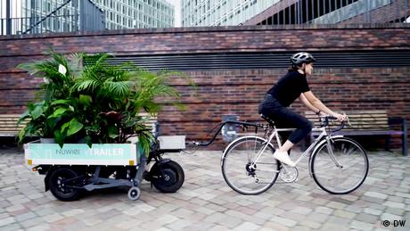 Eine Person zieht mit dem Fahrrad einen Anhänger, auf dem sich Pflanzen befinden (Quelle: DW)