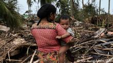 A Rohingya woman carries her baby next to her destroyed house at Basara refugee camp in Sittwe on May 16, 2023, after cyclone Mocha made a landfall. The death toll in cyclone-hit Myanmar's Rakhine state rose to at least 41 on May 16, 2023, local leaders told AFP. (Photo by SAI Aung MAIN / AFP)