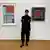Ukrainian art curator Yuliia Berdiiarova, dressed all in black and wearing glasses, stands in front of two artworks hanging on the wall at Museum Ludwig, Cologne on May 2023.
